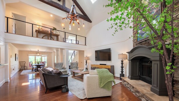 A spacious living room with a fireplace, a dining area, and a staircase leading to an upper level. - Welcome to this spectacular home, which stands out for its soaring stone fireplace, a bright sunroom, and a unique indoor-outdoor entertainment lounge with a classic arcade game! (Elliston)