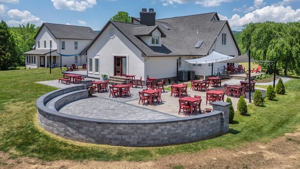 Talo, jossa on patio, ja patiolla on punaisia pöytiä ja tuoleja. Patiota ympäröi kivimuuri.