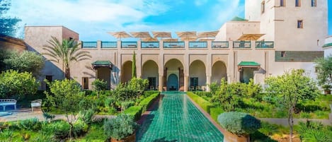Une cour avec une piscine, des palmiers et un bâtiment doté d’arcades et d’un balcon.