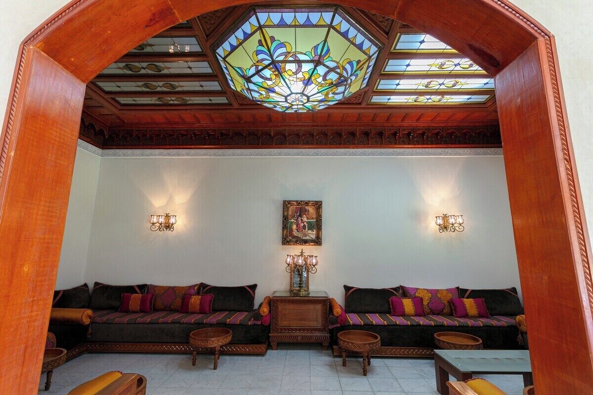 A room with a large stained glass window, two sofas with patterned cushions, a small table, and wall-mounted lamps.