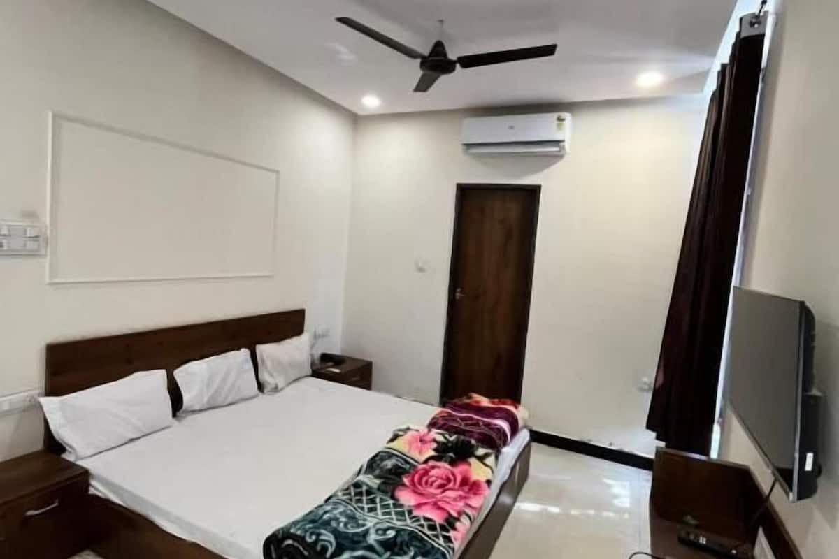Ein Schlafzimmer mit Bett, Deckenventilator, Klimaanlage, Fernseher und Nachttisch aus Holz.