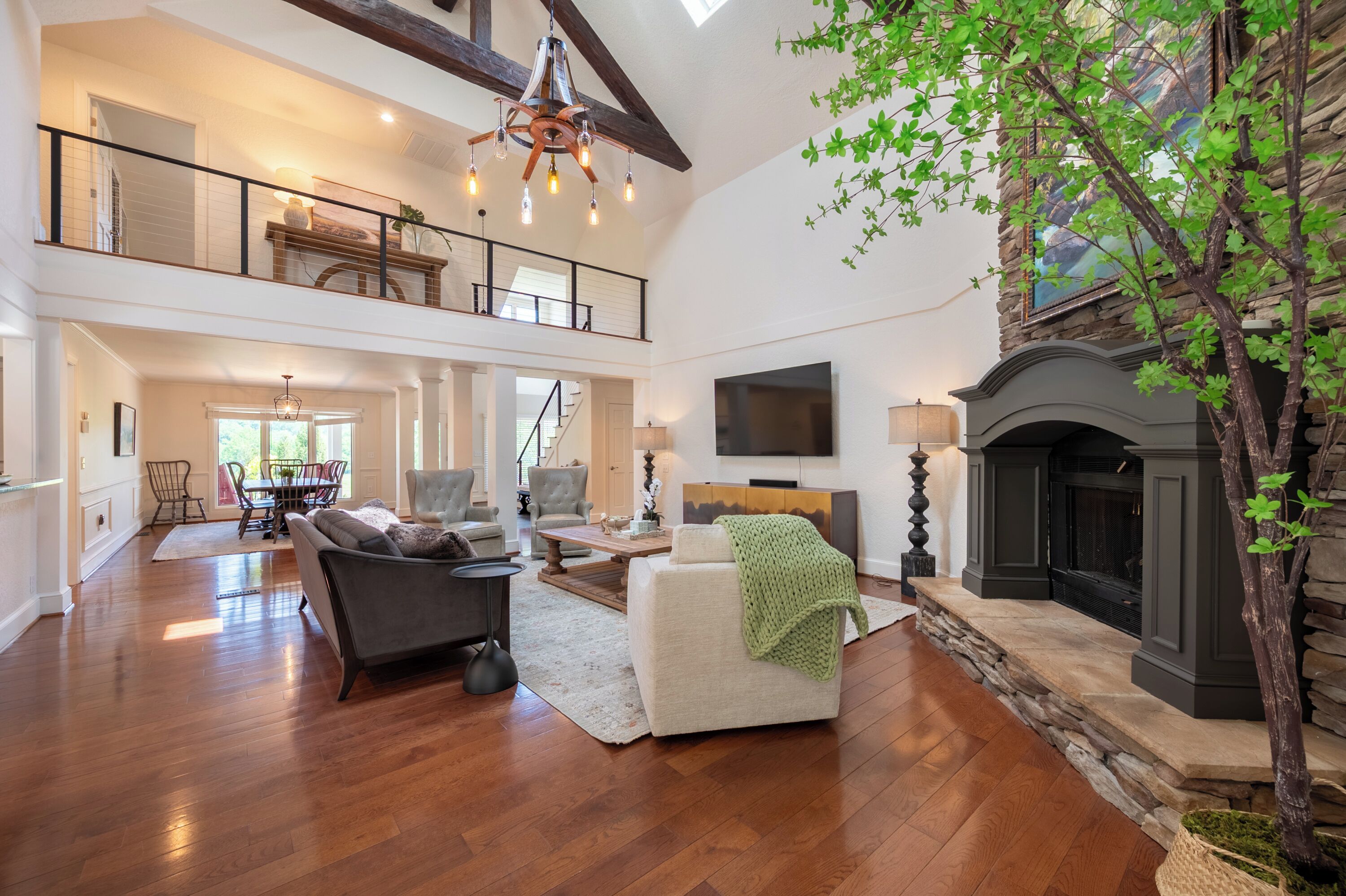 This stunning open-concept living room centers around a stone fireplace, featuring soaring vaulted ceilings and an elegant second-floor.
