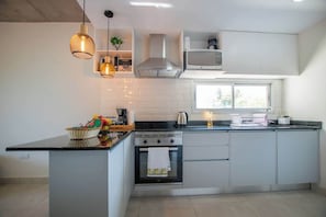 Eine moderne Küche mit Kochinsel, integriertem Backofen, Edelstahl-Dunstabzugshaube und Pendelleuchten.