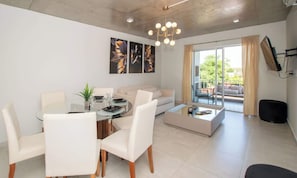 Ein modernes Wohnzimmer mit einem Glastisch, weißen Sofas und einem großen Fenster mit Vorhängen.