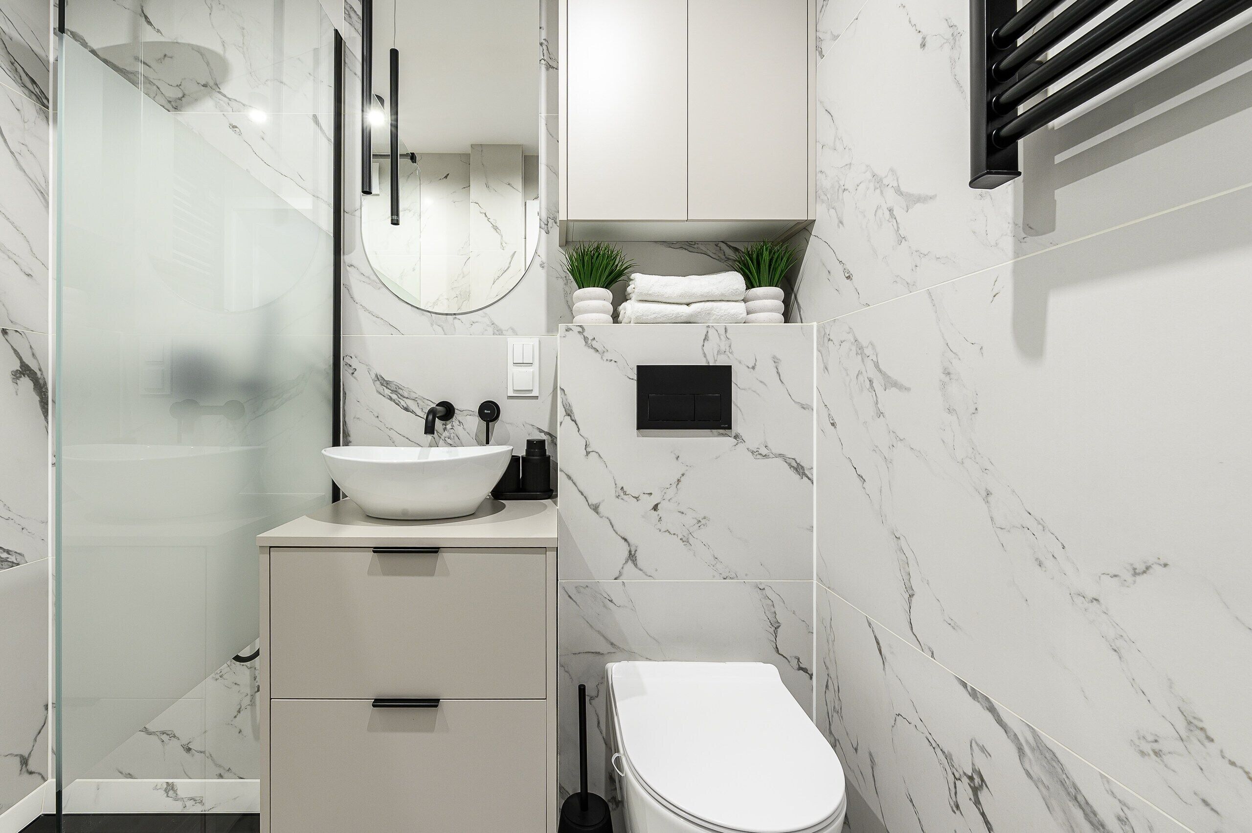 Et moderne badeværelse med en hvid vask, spejl og toilet, marmorvægge og en glasbrusekabine.