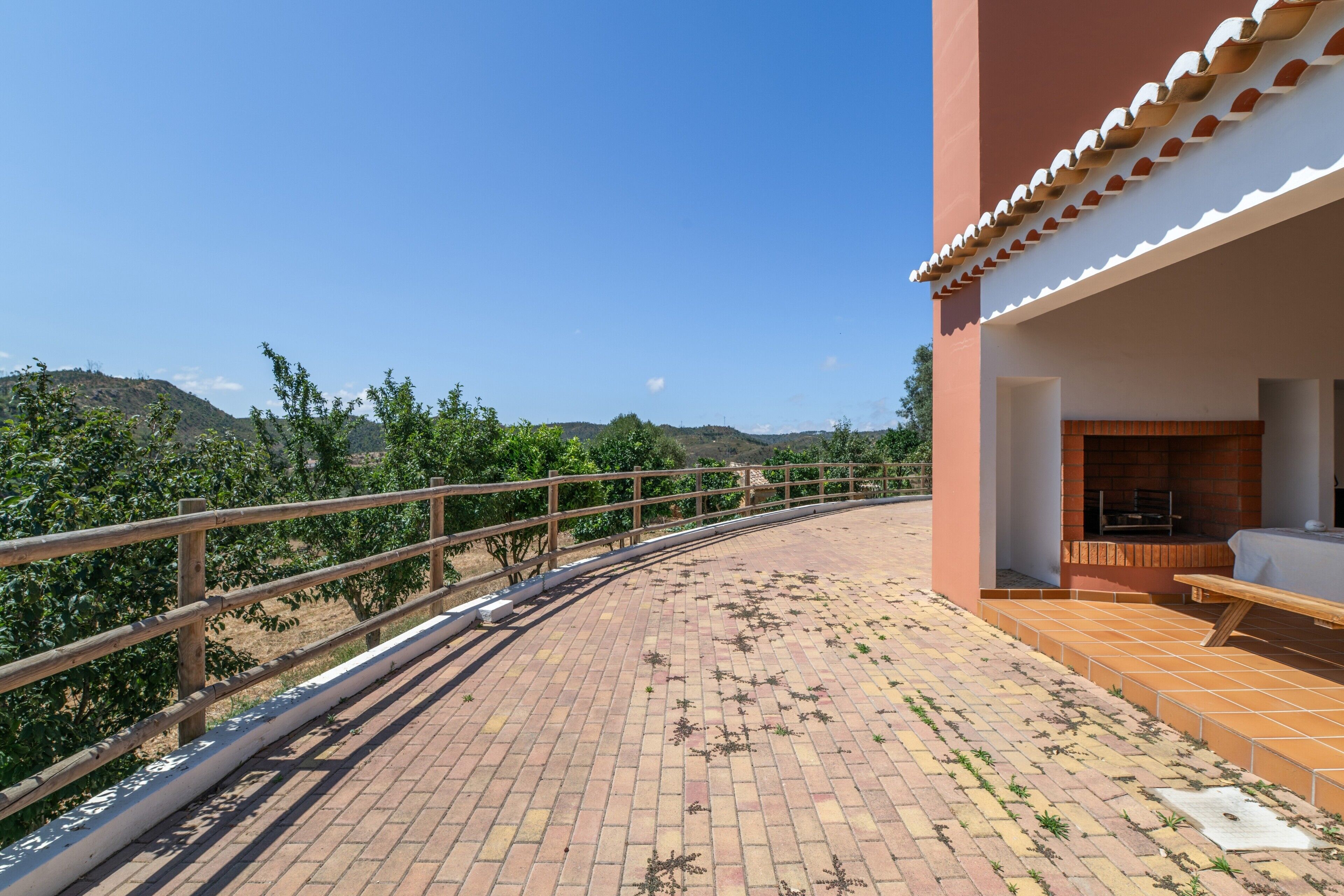 A rooftop terrace with a brick floor, a wooden railing, and a view of distant hills.