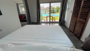 Ein Schlafzimmer mit einem großen Bett, einer Glastür, die auf einen Balkon mit Blick auf einen Pool führt.