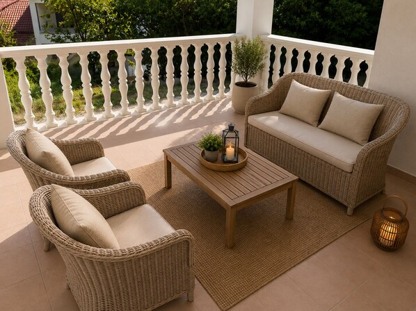 Een balkon met rieten meubels, een houten tafel en een plant in pot.