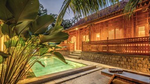 A swimming pool with steps leading to a wooden building, surrounded by tropical plants. - Omah Nyang Uluwatu (Uluwatu)