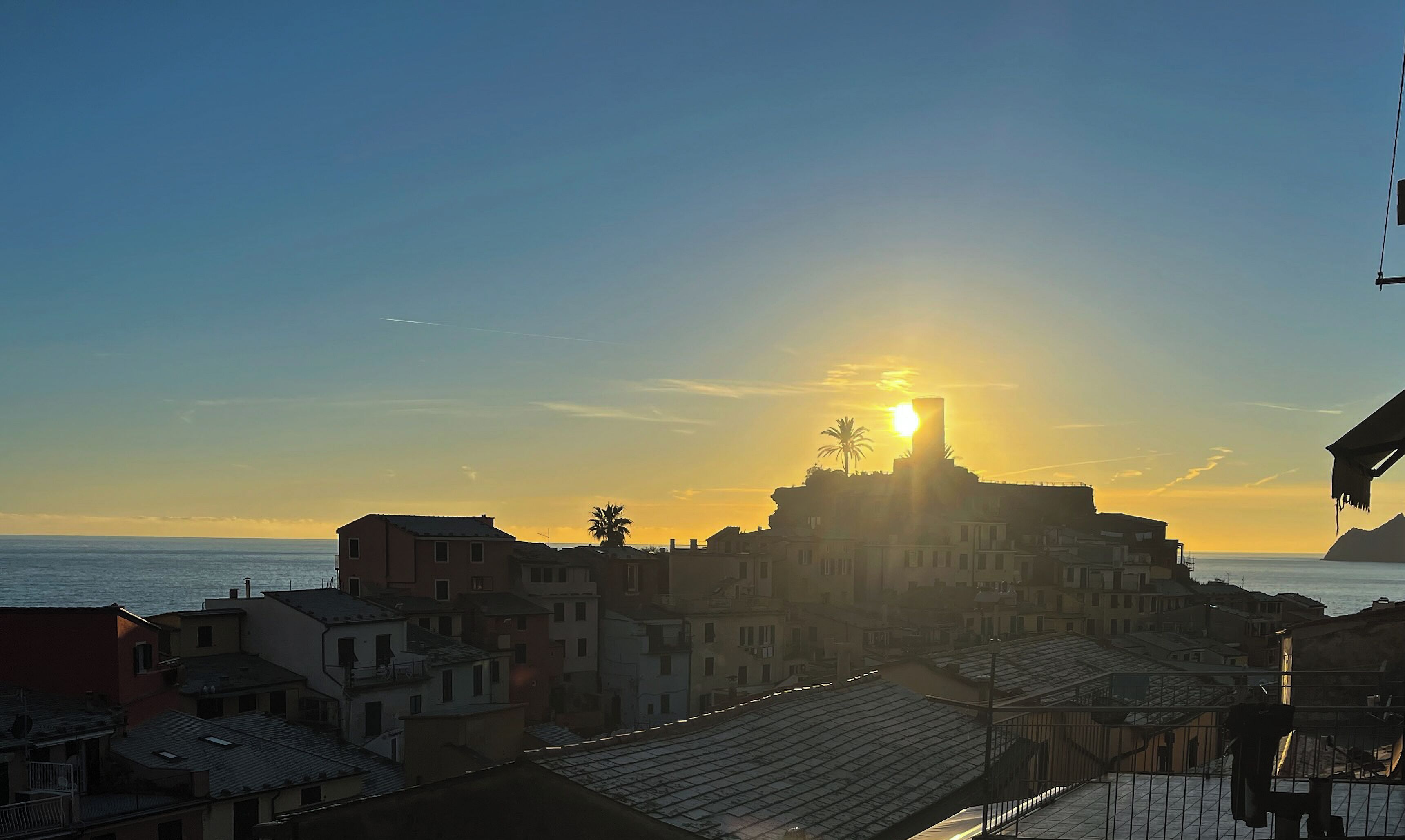 Un pueblo costero con edificios y una torre destacada silueteada contra el sol poniente.