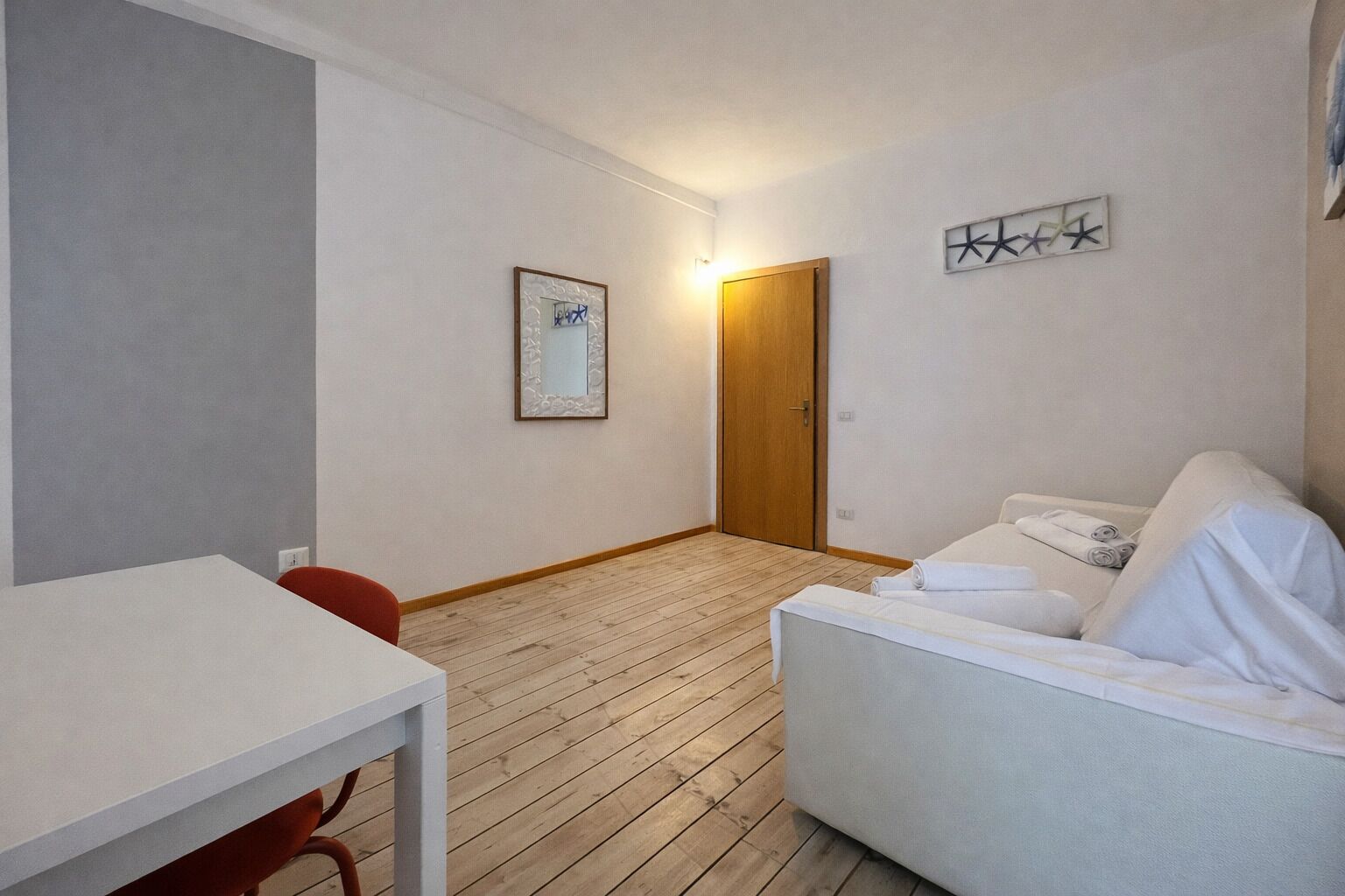 A hotel room with a wooden floor, a white sofa, a small table, and a door.