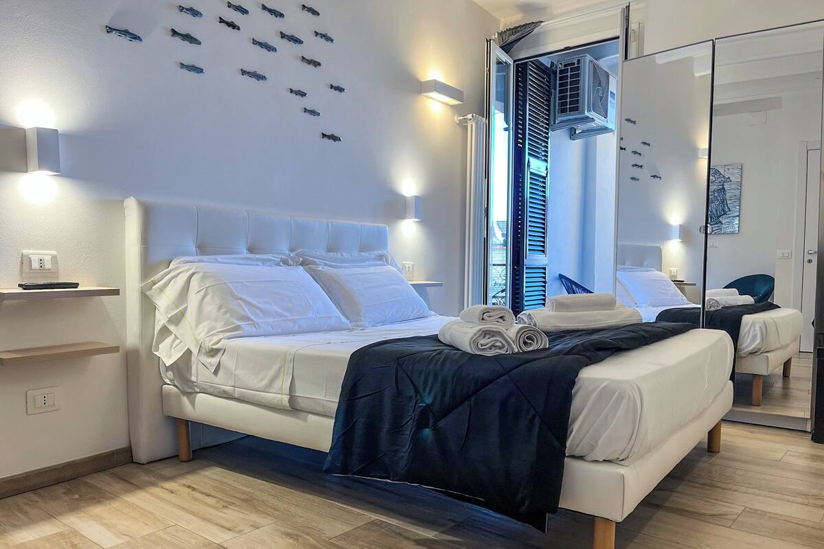 A modern hotel room with a large bed, bedside tables, a mirror, and a view of the outside.