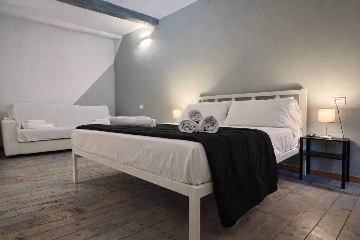 A bedroom with a bed, a nightstand, a lamp, and a sofa.