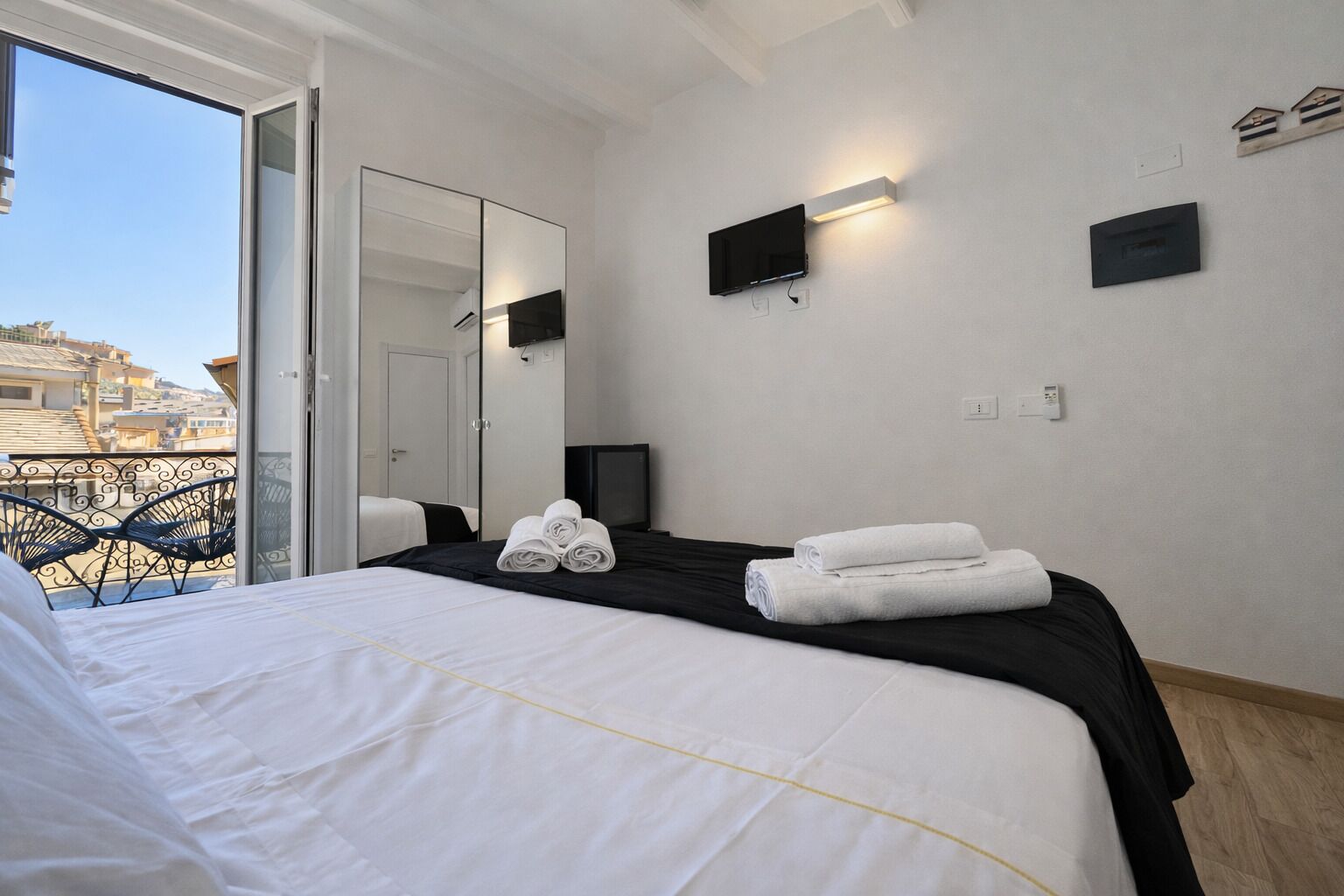 Une chambre d’hôtel avec un lit, une télévision, un miroir et un balcon équipé de chaises.