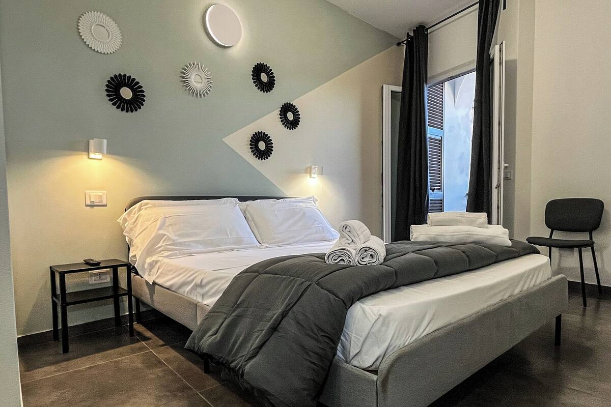 A modern bedroom with a bed, a chair, a nightstand, and wall decor.