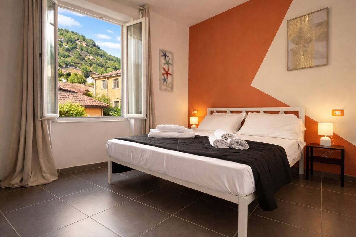 A hotel room with a bed, two bedside tables, a window with curtains, and a view of a hillside.