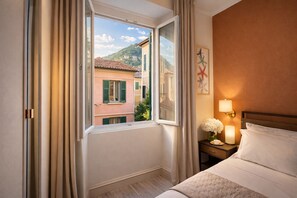 Une chambre d’hôtel avec un lit, une table de chevet avec une lampe, une fenêtre avec des rideaux et une vue sur les bâtiments environnants.