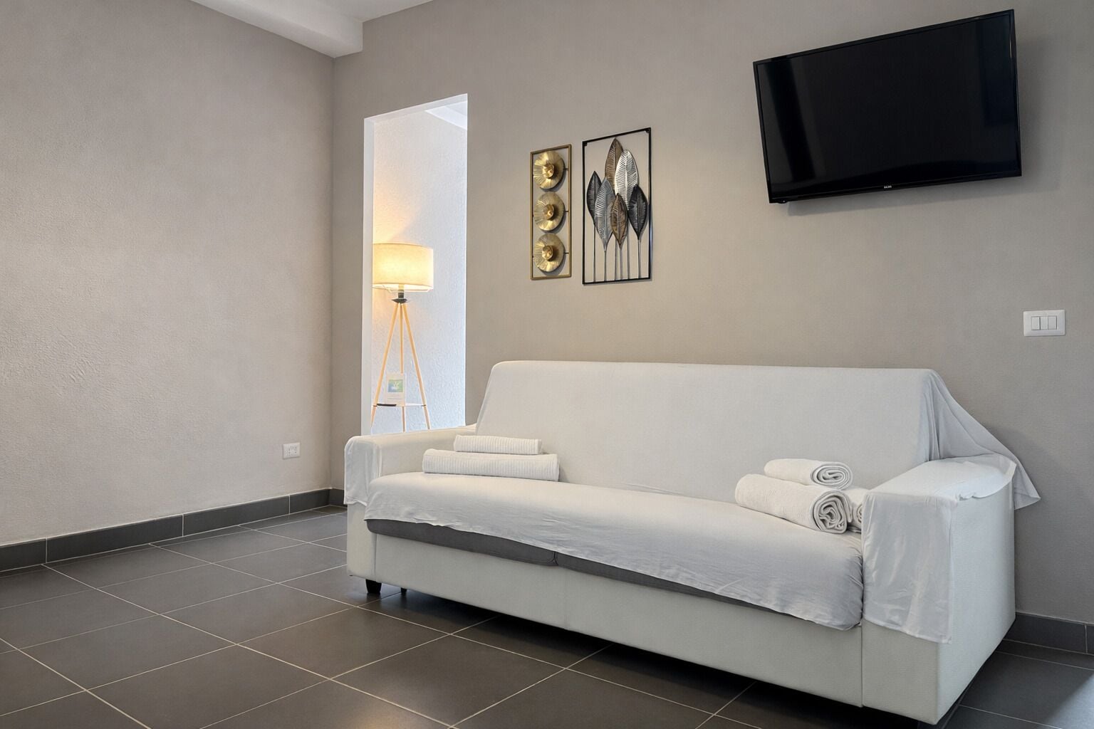 A modern room with a white sofa, a flat-screen TV, and two wall art pieces.