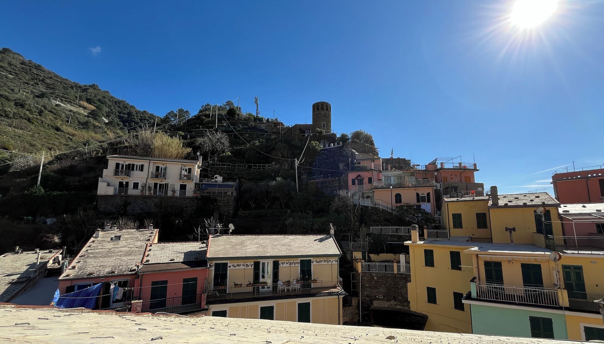 A coastal village with buildings on a hillside, a prominent tower, and a clear blue sky.