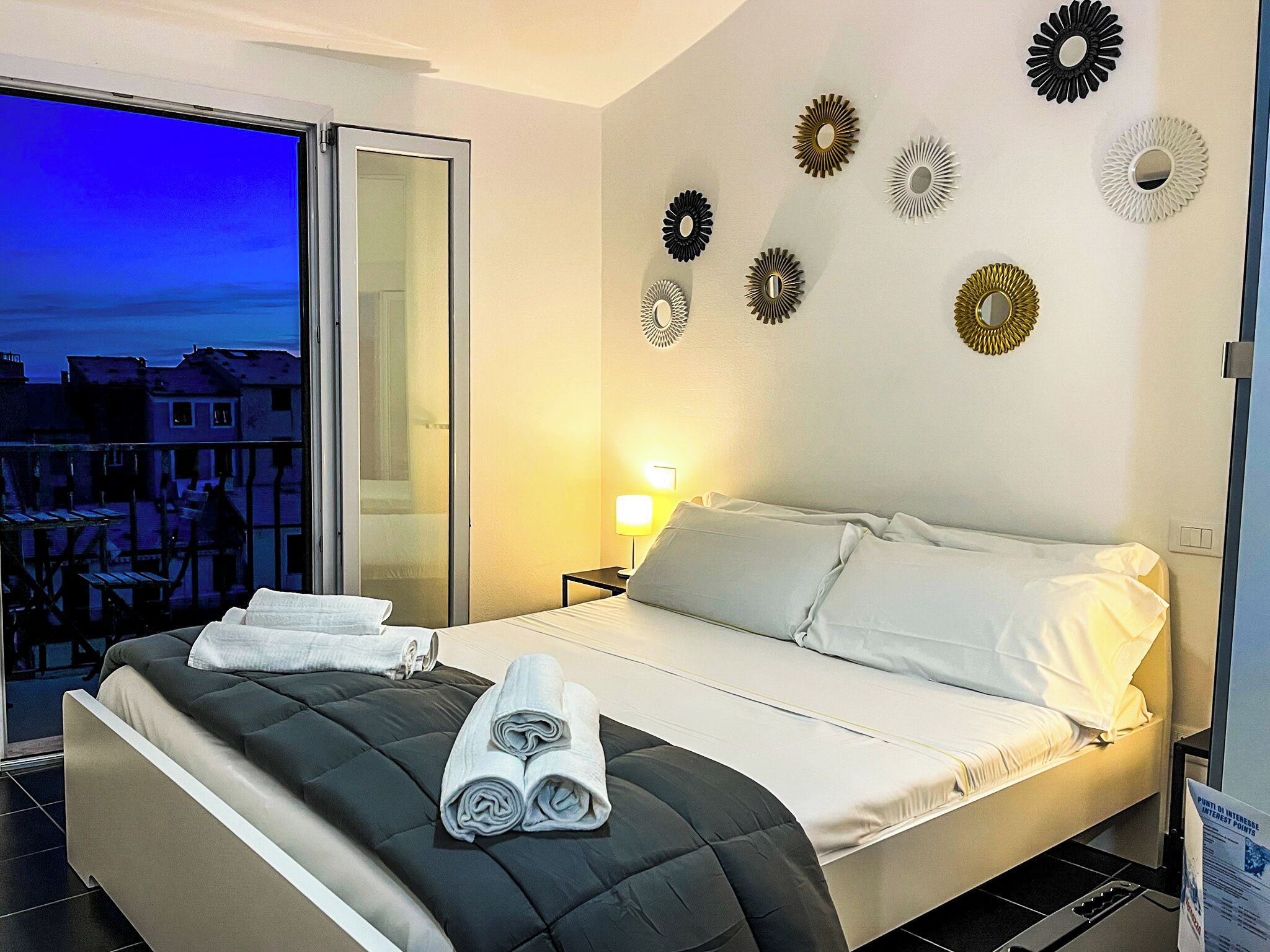 Ett hotellrum med en säng, en balkong med utsikt och dekorativa väggspeglar.