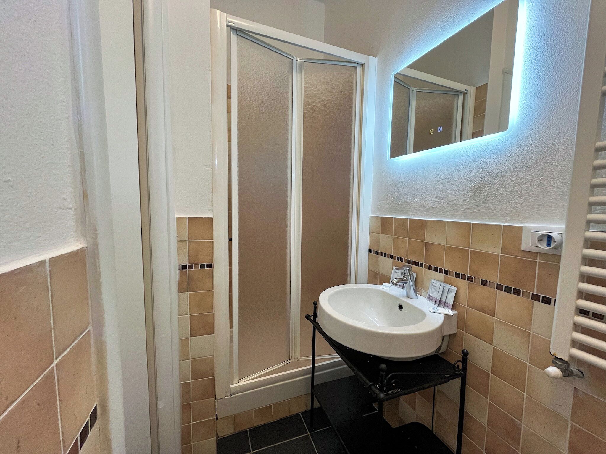 A bathroom with a shower, a sink, a mirror, and a towel rack.