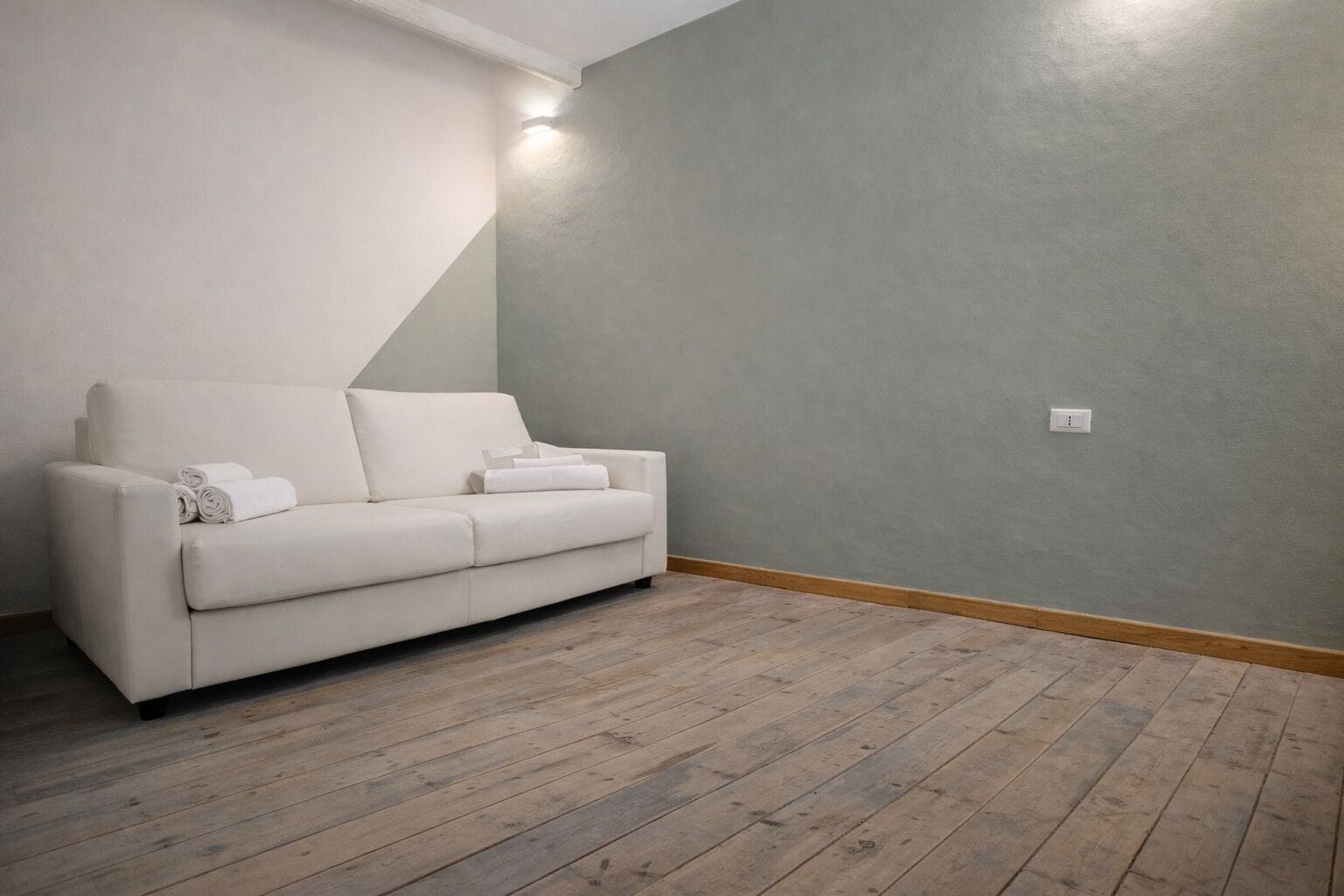 Una habitación con un sofá blanco, suelo de madera y pared gris.