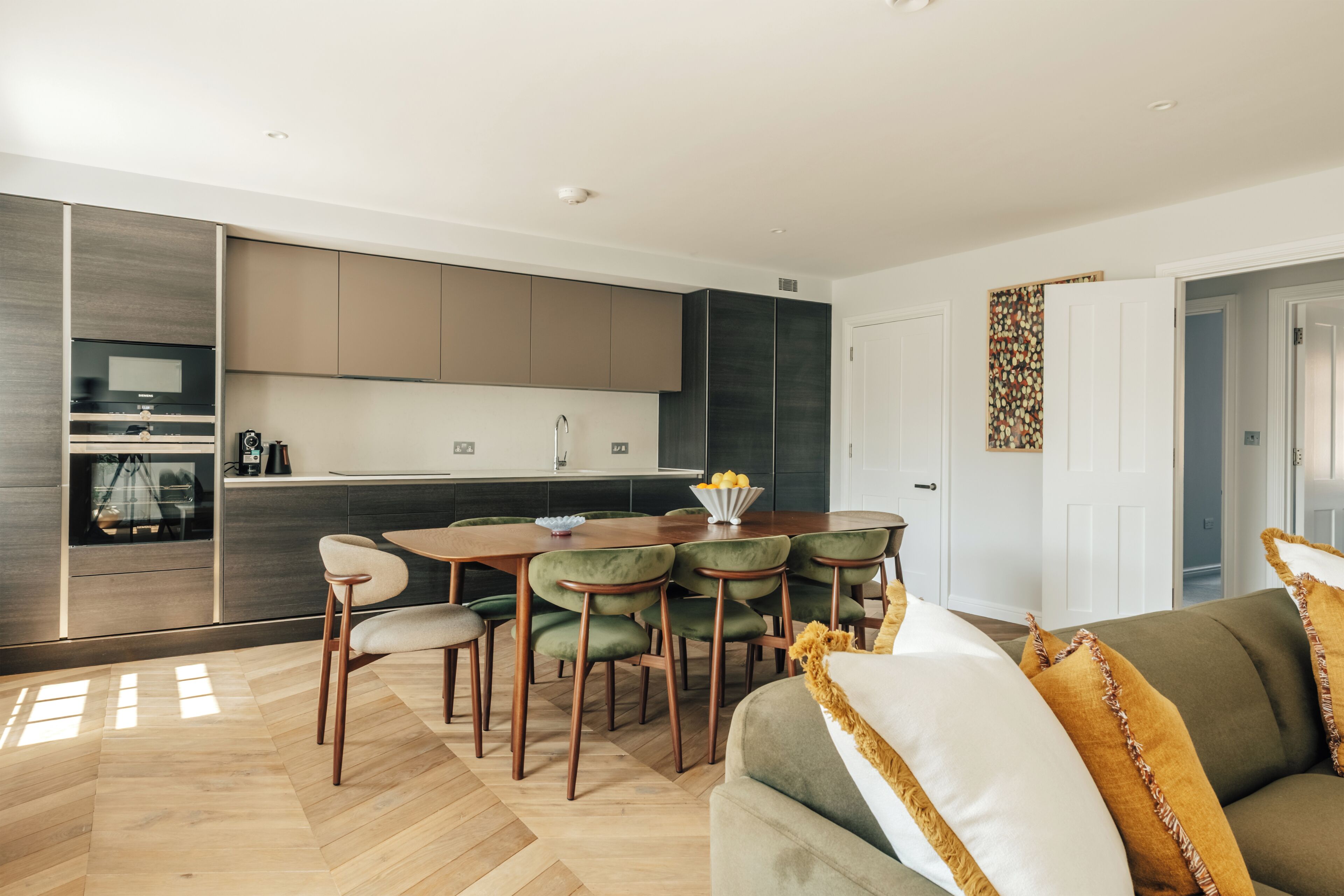 A modern kitchen with a dining area, wooden flooring, and a sofa with decorative pillows.
