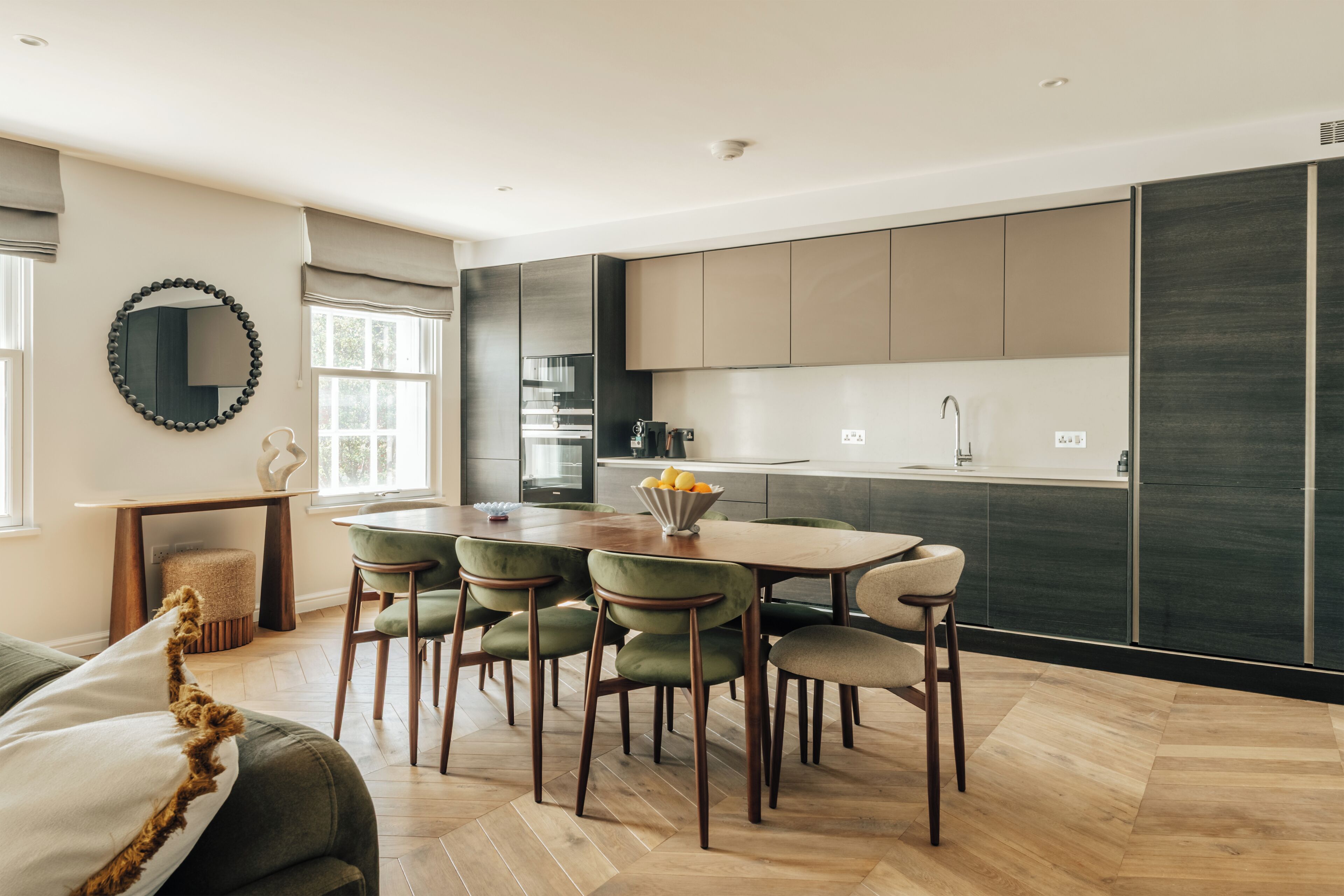 Een moderne keuken met een eethoek, houten vloeren en een ronde spiegel aan de muur.