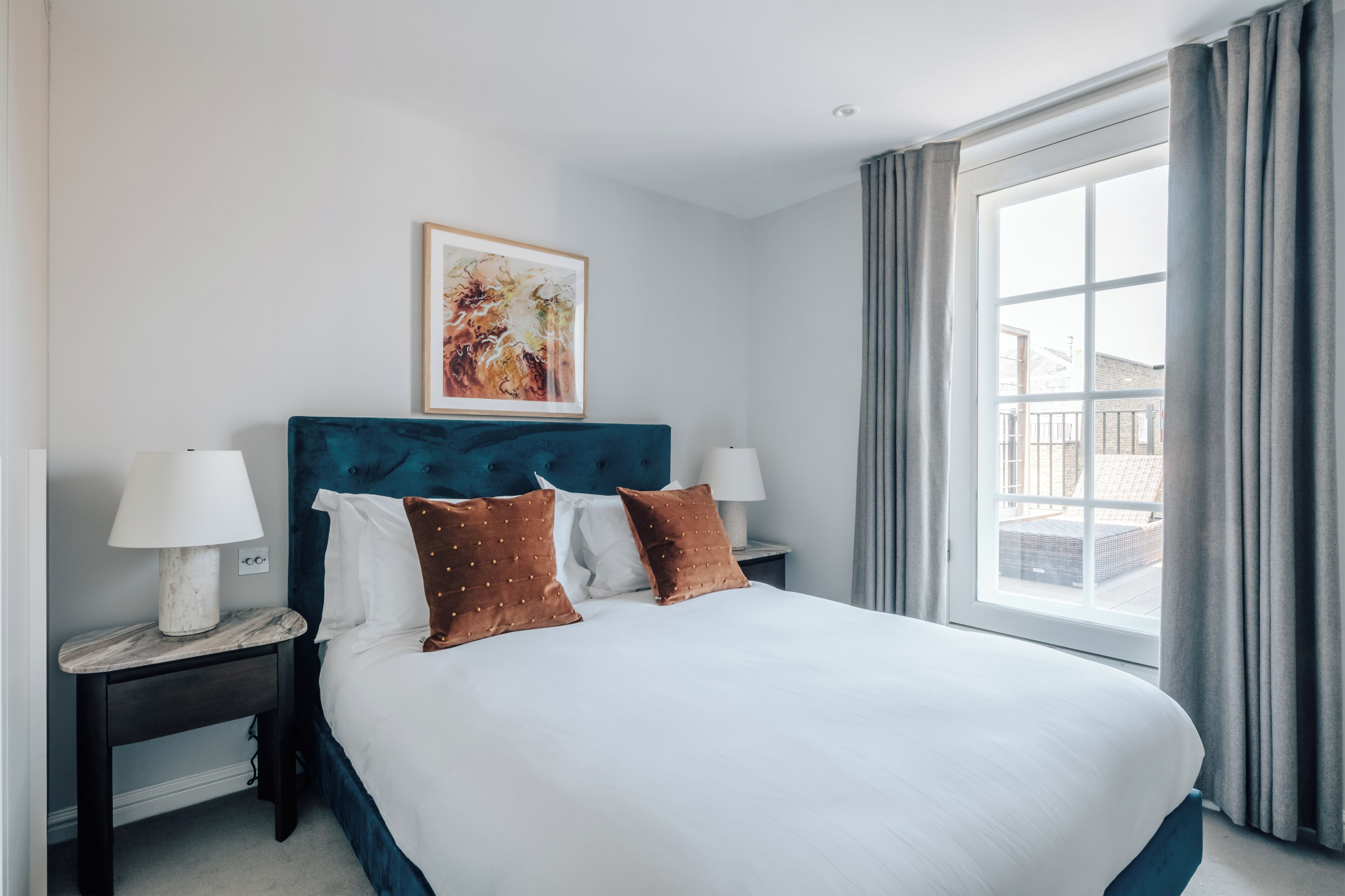 Une chambre d’hôtel avec un grand lit, deux tables de chevet avec des lampes, une œuvre d’art encadrée au-dessus du lit et une vue dégagée sur l’extérieur grâce à une grande fenêtre.