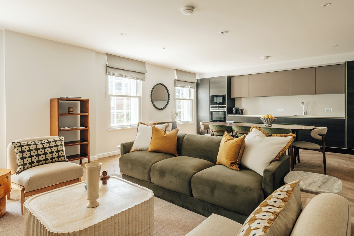 Ein modernes Wohnzimmer mit einer Couch, Sesseln, einem Couchtisch und einem Bücherregal.