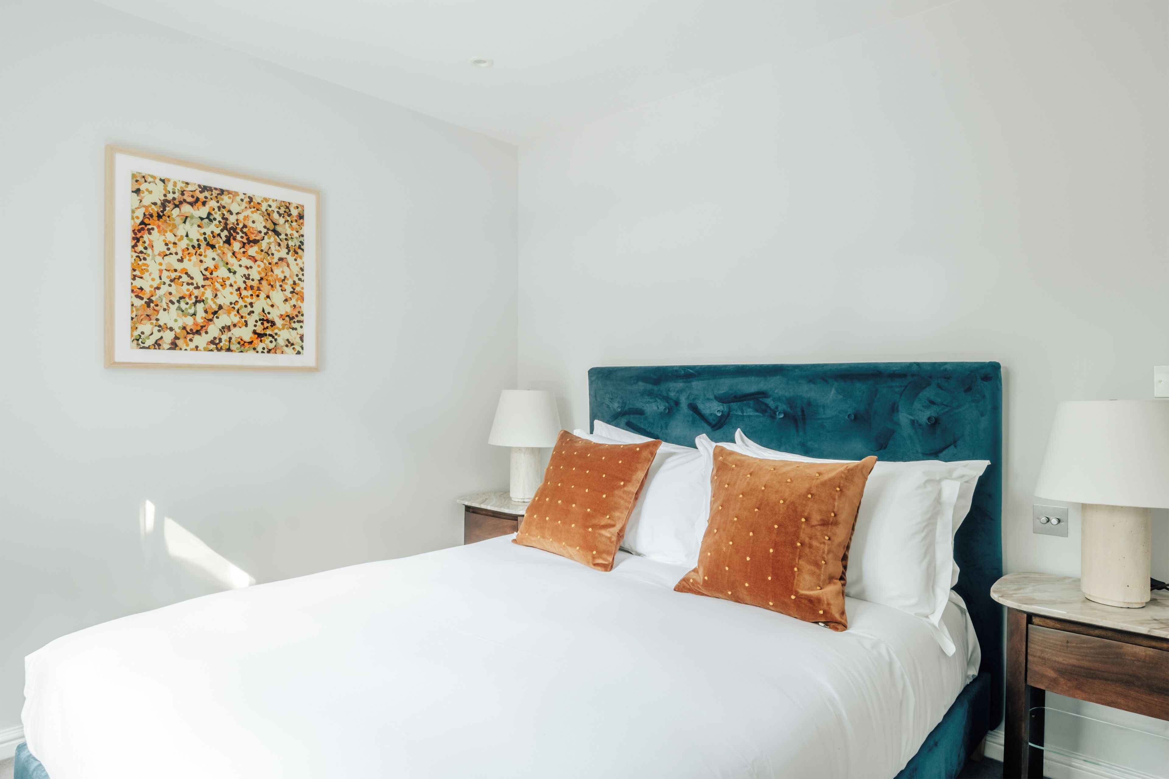 A neatly made bed with white and brown pillows, a teal headboard, and a framed artwork on the wall.