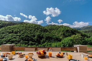 Ein Tisch reichhaltig mit Frühstück zubereitet und Blick auf einen bewaldeten Berg.