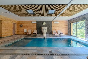 A modern indoor pool with wooden walls, stone accents, and a large sculptural centerpiece.