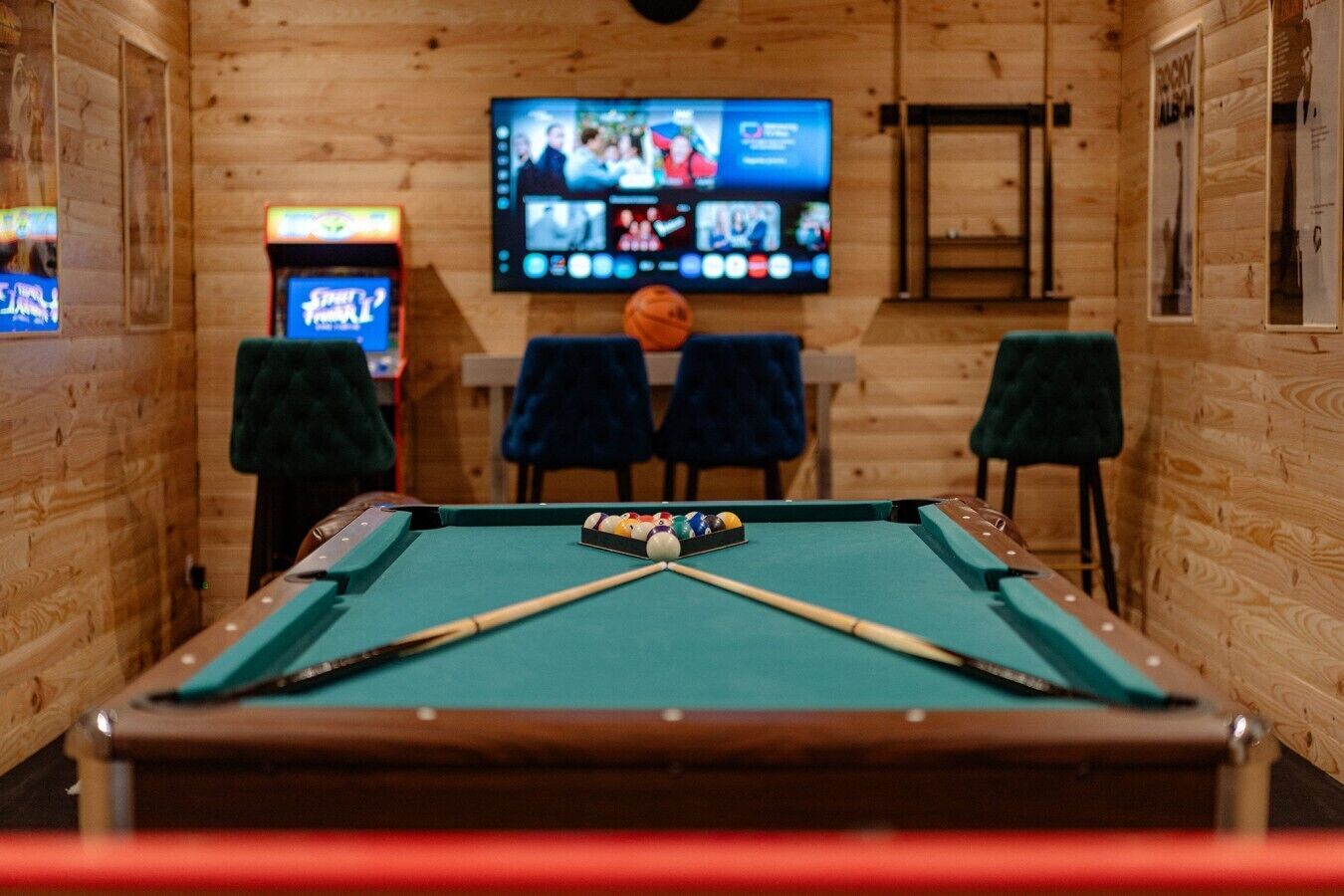 Une table de billard recouverte d’un drap vert, deux chaises et un téléviseur fixé au mur qui diffuse plusieurs chaînes.