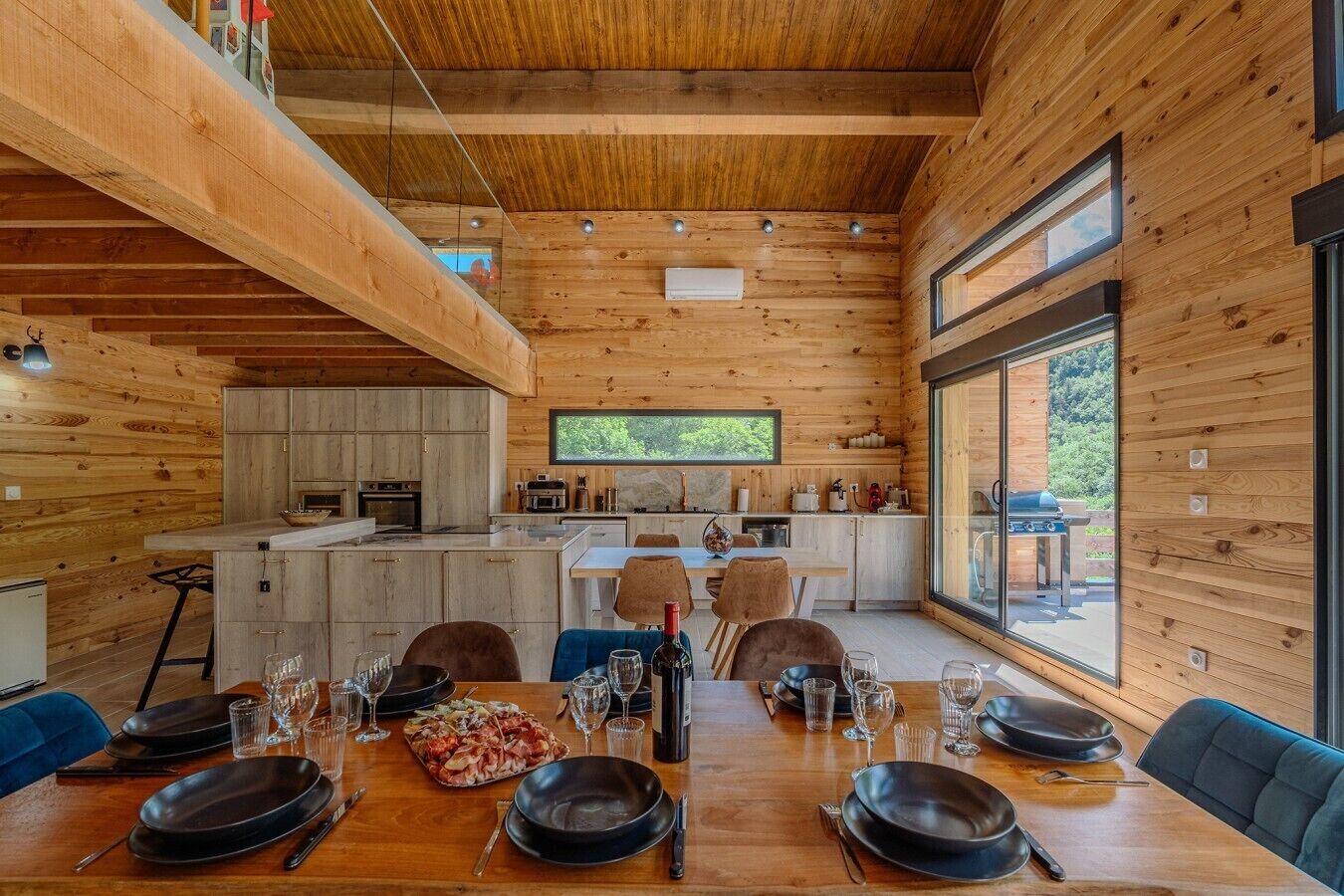 Une maison en rondins moderne dotée d’un coin repas, d’une cuisine et de grandes fenêtres.