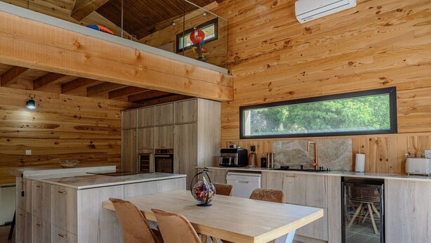 A modern kitchen with wooden walls, a large window, and a dining area with a table and chairs. - L'Écrin Secret Chalet•Swimming Pool•Mountain View•12pers (Fontpédrouse)