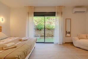Ein Schlafzimmer mit einem Bett, einer Schlafcouch, einer Schiebetür zu einem Garten und einer Klimaanlage.