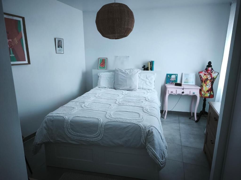 Une chambre à coucher comprenant un lit, une table de chevet, une commode et un luminaire suspendu.