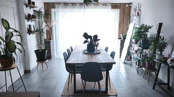 Un coin repas avec une table en bois, des chaises, des plantes en pot et une vue à travers une porte vitrée.