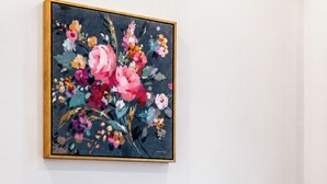 Een slaapkamer met een bed, kussens en een wanddecoratie met bloemen.
