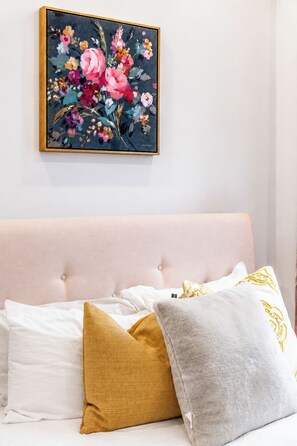 Ein Schlafzimmer mit einem Bett, Kissen und einem gerahmten Blumenbild an der Wand.