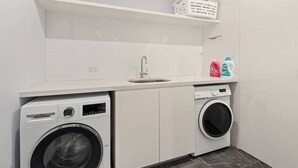 Een kleine wasruimte met een Bosch wasmachine, een voorlader droger, een wasbak en een plank met wasmanden en schoonmaakmiddelen.