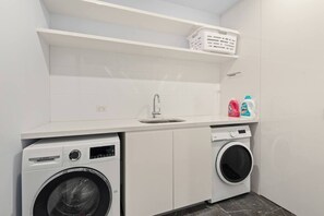Ein kleiner Hauswirtschaftsraum mit einer Bosch Waschmaschine, einem Vorlader Trockner, einem Waschbecken und einem Regal mit Wäschekörben und Reinigungsmitteln.
