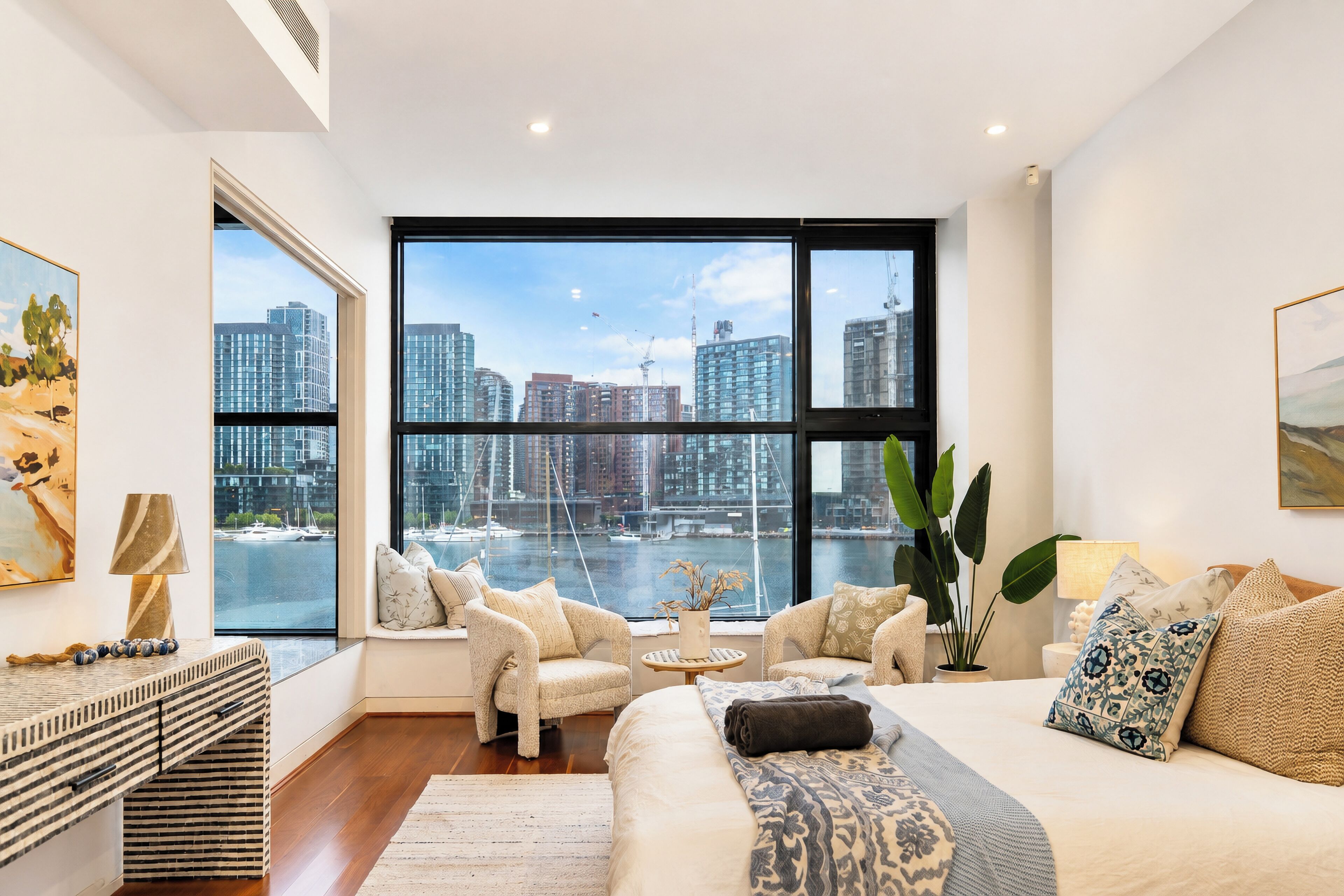 A modern living room with a large window, a sofa, a coffee table, and a view of the city skyline.
