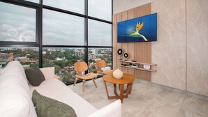 Una sala de estar moderna con un ventanal grande, un sofá, dos sillones, una mesa redonda y un televisor montado.