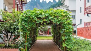 A pathway leading through a vine-covered archway in a courtyard with buildings in the background. - Zhangjiajie New Pipaxi Courtyard Hotel (Zhangjiajie)