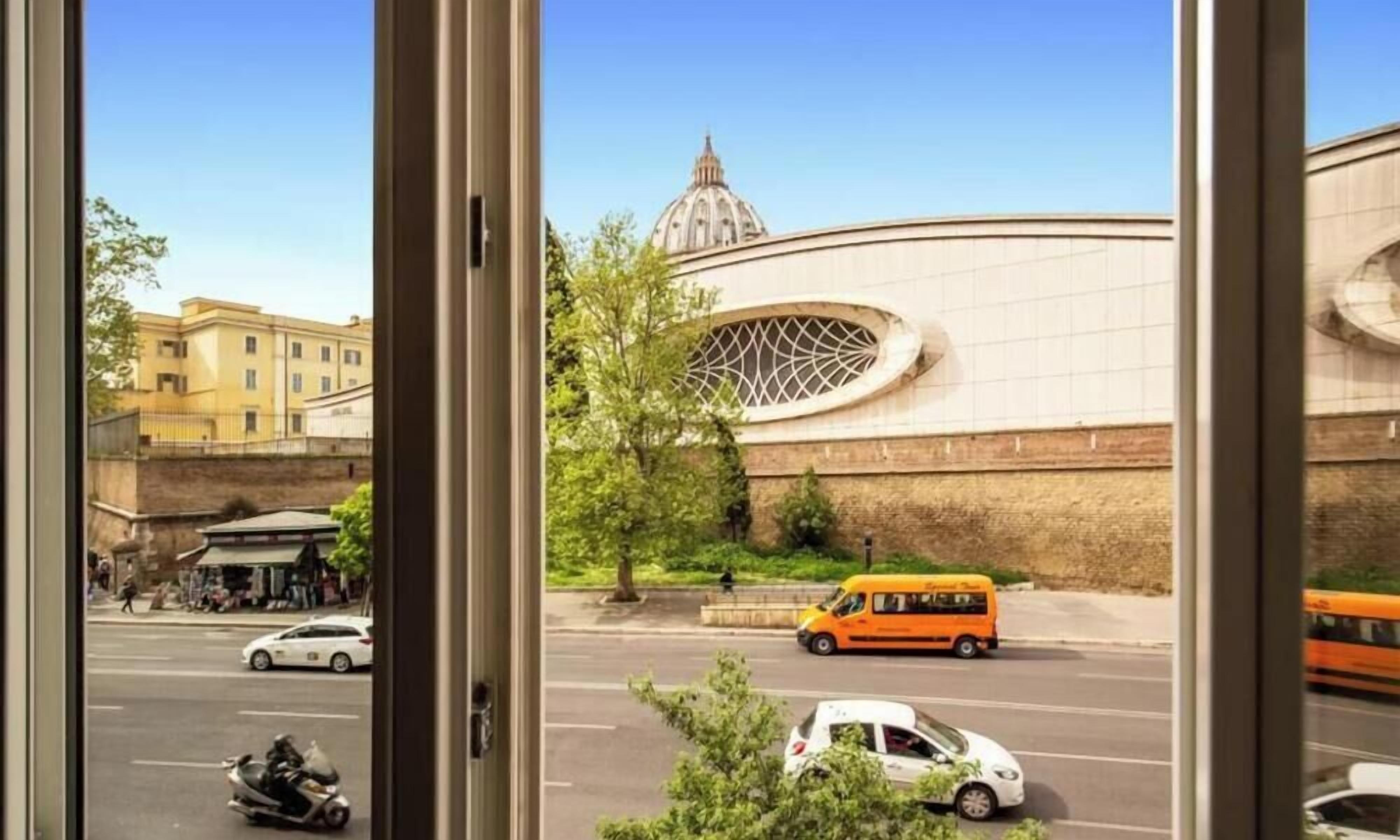 Vista a través de una ventana de una calle con un edificio moderno de grandes dimensiones, con cúpula y fachada curva.