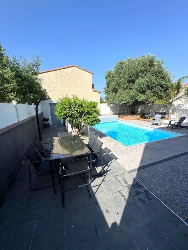 Un jardin avec une piscine, une table et des chaises, et un petit arbre.