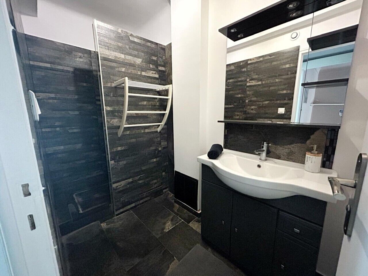 Une salle de bain moderne avec une douche à parois de verre, un lavabo blanc, des meubles de couleur sombre et un miroir au-dessus du lavabo.