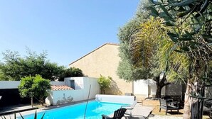 Un giardino sul retro con piscina, zona barbecue e piante in vaso.